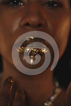 Portrait of a young African American woman with a gold necklace around her neck. Liquid gold is applied to the models