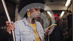 Portrait of young african american woman with headphones listening to music, sing and funny dancing in public transport
