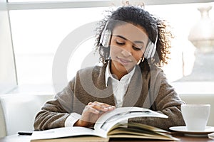 Portrait of young african american woman reading book on sofa in cafe