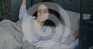 Portrait of young African American woman sleeping then waking up stretching arms in bed at home