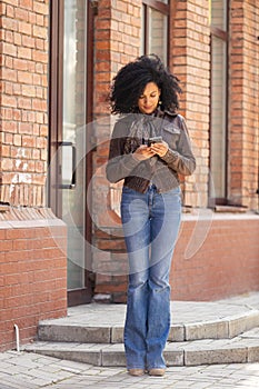 Portrait of young African American woman texting on her smartphone. Brunette with curly hair in leather jacket and