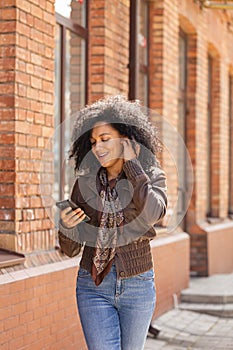 Portrait of young African American woman texting on her smartphone and smiling. Brunette with curly hair in leather
