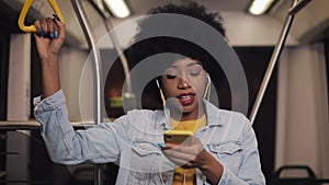 Portrait of young african american woman wearing i with headphones listening to music, sing and funny dancing in public