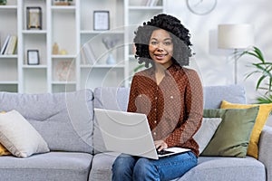 Portrait of a young African American woman working and studying at home. Sitting on the couch, holding a laptop on his