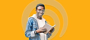 Portrait of young african man student with book looking at camera wearing eyeglasses isolated on yellow background