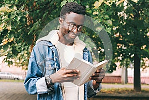 Portrait young african man student reading a book wearing an eyeglasses in autumn city park