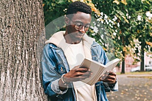 Portrait young african man student reading a book wearing an eyeglasses in autumn city park