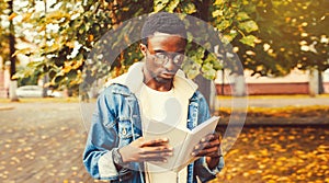 Portrait of young african man student reading a book wearing eyeglasses in autumn city park