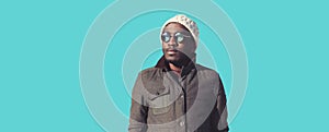 Portrait of young african man wearing sunglasses, winter hat, jacket on sky background