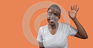 Portrait of young African woman looking at camera and waving hand with big smile against orange background