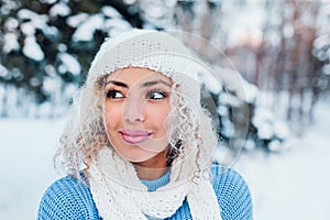 Portrait of young afro american girl wearing hat, blue sweater posing in winter park.