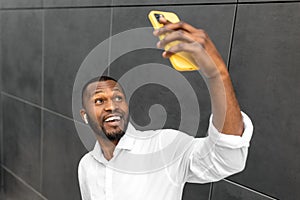 Portrait of young afro american male taking selfies with his mobile phone isolated on grey background outdoors. Handsome