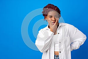 Portrait of young afro woman with bored face expresison touching her chin against blue background
