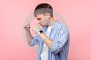 Portrait of young aggressive brown-haired man standing with clenched fists, ready to punch. isolated on pink background