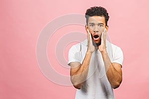 Portrait of young amazed man with afro hairstyle in white t-shir, looking in camera with opened mouth and shocked expression