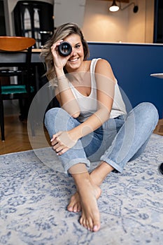 Portrait of young amazing woman photographer sitting with crossed legs, holding, looking through modern camera lens.