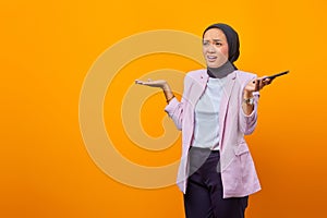 Portrait of young angry asian woman raising palms confusedly isolated over yellow background
