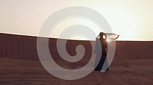 Portrait of a young Arab woman wearing traditional black clothing during beautiful sunset over the desert.