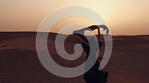 Portrait of a young Arab woman wearing traditional black clothing during beautiful sunset over the desert.