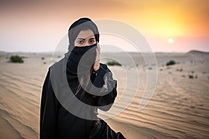 Portrait of a young Arab woman wearing traditional black clothing during beautiful sunset over the desert