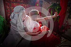 Portrait of young arabian muslim couple in traditional clothes in cozy red room. Fhoto shoot in easten style with male