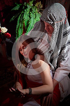 Portrait of young arabian muslim couple in traditional clothes in cozy red room. Fhoto shoot in easten style with male