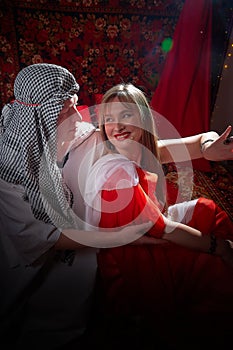 Portrait of young arabian muslim couple in traditional clothes in cozy red room. Fhoto shoot in easten style with male