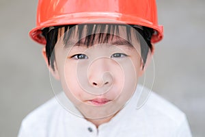 Portrait of Young Asia boy in gray T shirt wearing a orange safety helmet in the garden at home