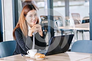 Portrait of young Asian business woman at the cafeteria with a laptop having a coffee break and looking at camera. Enjoying work