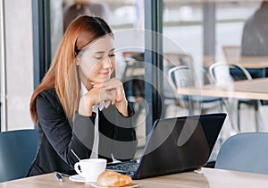 Portrait of young Asian business woman sitting at cafeteria with laptop. Woman taking a break. Enjoying work from coffee shop.