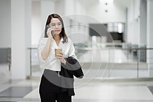 Portrait of a young Asian business woman talking over cellphone and holding cup of coffee in business building. Fashion business