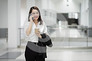 Portrait of a young Asian business woman talking over cellphone and holding cup of coffee in business building. Fashion business