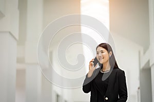 Portrait of a young Asian business woman talking over cellphone and holding cup of coffee in business building. Fashion business