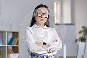Portrait of a young Asian business woman, a worker in the office with crossed arms looking at the camera