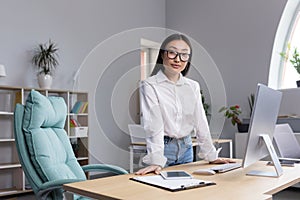 Portrait of a young Asian businesswoman in the office. She leans on the table with her hands