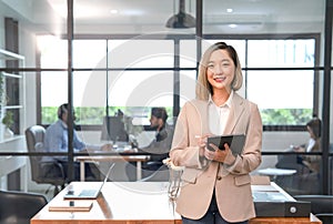 portrait young asian businesswoman smiling,holding digital tablet,standing in the office room