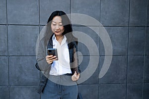 Portrait of Asian businesswoman using mobile phone while standing against wall outdoors