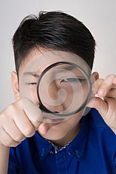 portrait of a young asian child looking through a magnifying glass