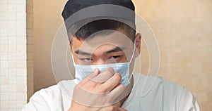 Portrait of a young asian cook man in uniform putting on a protective mask and looking at the camera
