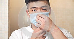 Portrait of a young asian cook man in uniform putting on a protective mask and looking at the camera.