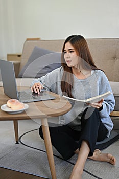 Portrait, Young Asian female sits on the living room floor, using laptop computer