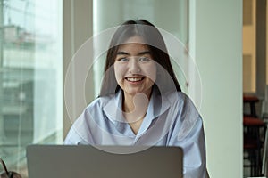 Portrait young asian girl looking camera while using laptop computer