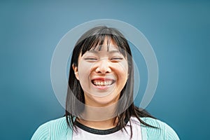 Portrait of young Asian girl smiling at camera - Happy Chinese woman having fun posing against blue background