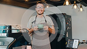 Portrait young Asian guy barista waitress holding coffee cup feeling happy at urban cafe. Asia small business owner boy in apron