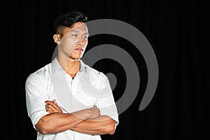 Portrait of a young asian handsome boy wearing white shirt crossing hands on the black background. Sadness expression feeling