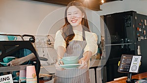 Portrait young Asian lady barista waitress holding coffee cup feeling happy at urban cafe. Asia small business owner girl in apron
