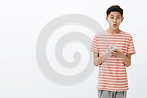 Portrait of young asian male adolescent with cool hairstyle in striped t-shirt holding smartphone being excited using
