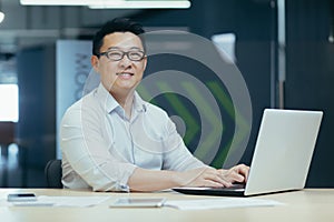 Portrait of a young Asian male architect, engineer in glasses working in the office, sitting at the table at the laptop