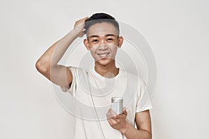 Portrait of young asian man with problematic skin and hyperpigmentation on his face smiling at camera, holding cream jar