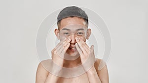 Portrait of young asian man with problematic skin and hyperpigmentation looking at camera, applying cream on his face